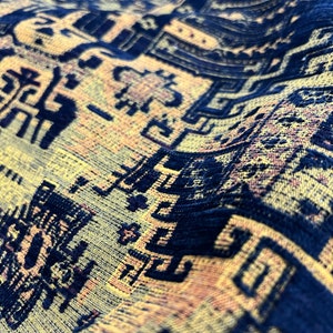 May include: Close-up of a blue and yellow patterned fabric with a textured surface. The fabric has a repeating geometric design.
