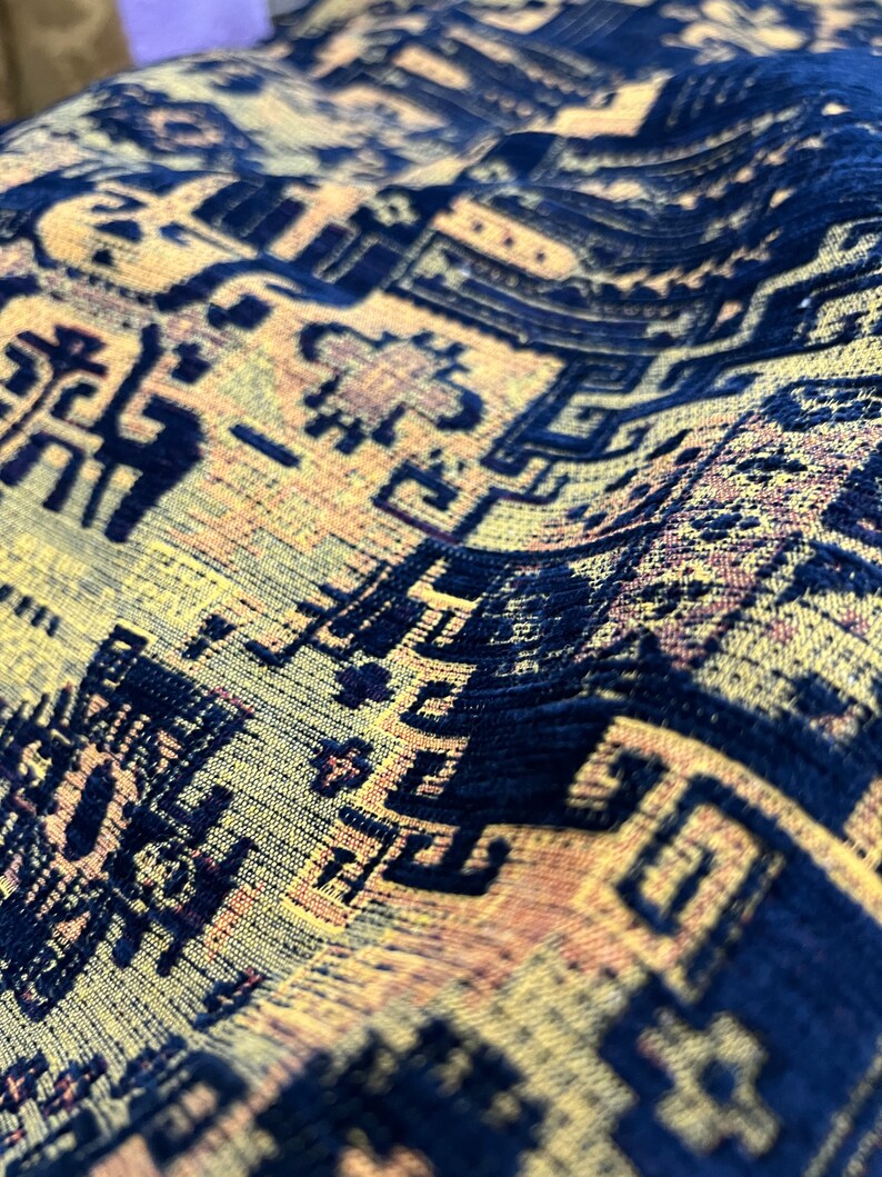 May include: Close-up of a blue and yellow patterned fabric with a textured surface. The fabric has a repeating geometric design.