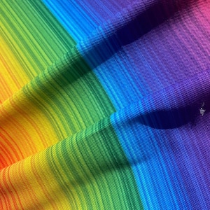 Könnte beinhalten: Ein regenbogenfarbener Stoff mit strukturierter Oberfläche. Der Stoff ist in der Mitte gefaltet und bildet eine diagonale Linie über das Bild.