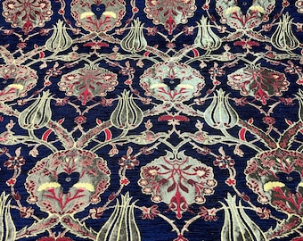 May include: A close-up of a blue fabric with a repeating pattern of stylised flowers and leaves. The fabric has a textured, almost velvet-like appearance.