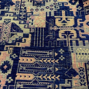 May include: A close-up of a fabric with a geometric pattern in shades of blue, yellow, and orange. The fabric has a textured surface and a woven appearance.