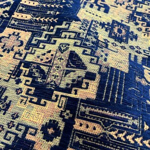 May include: Close-up of a blue and gold patterned fabric with a geometric design. The fabric has a textured surface and a woven appearance.