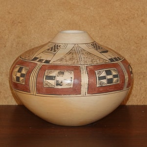 Puede incluir: Una olla de cerámica blanca con un diseño geométrico en negro y rojo. La olla tiene una forma redondeada y una abertura ancha.