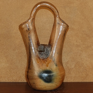 May include: A brown and black ceramic vase with two openings. The vase has a unique shape with a handle at the top.