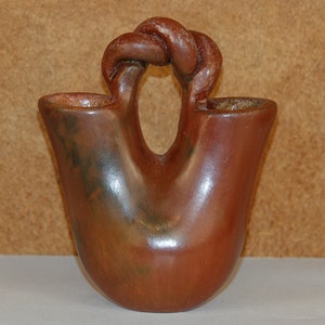 May include: A brown, hand-crafted, double-spouted pottery vase with a twisted handle.