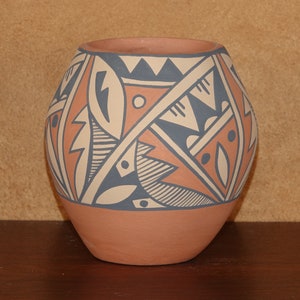 Op de afbeelding: Een traditionele Native American aardewerken vaas met een geometrisch ontwerp in tinten blauw, wit en oranje. De vaas is rond en heeft een brede opening.