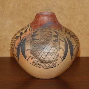 Puede incluir: Un pequeño jarrón de cerámica marrón redondo con diseños geométricos negros y rojos.