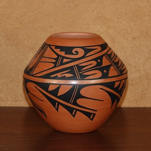 May include: A traditional Native American pottery vase with a black and brown geometric design. The vase is made of clay and has a rounded shape.