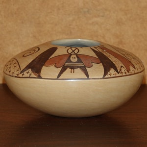 Puede incluir: Una olla de cerámica de color beige con un diseño geométrico marrón y rojo. La olla es redonda y tiene una abertura ancha.