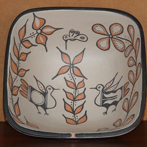 May include: A square ceramic bowl with a black rim and a white background. The bowl is decorated with a hand-painted design of stylized birds, flowers, and leaves in orange and black.