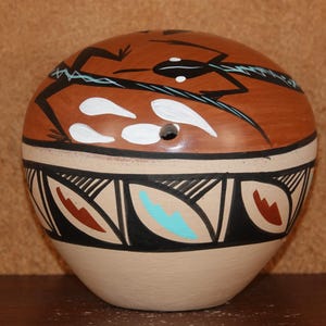 Può includere: Un vaso in ceramica dipinto a mano con un motivo geometrico marrone, bianco e nero. Il vaso presenta un motivo di uccello stilizzato nella parte superiore.