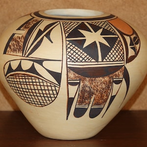 Puede incluir: Una olla de cerámica blanca con un diseño geométrico en negro y marrón. La olla tiene una forma redondeada y una boca ancha.