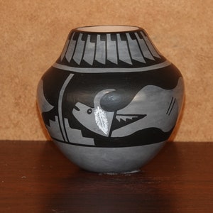 Könnte beinhalten: Ein grauer Keramiktopf mit schwarzen und weißen Designs. Der Topf zeigt ein stilisiertes Tierdesign mit einer Feder.
