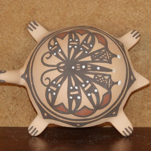May include: A hand-painted ceramic turtle with a brown, red, and white butterfly design. The turtle has a rounded shell and four legs.