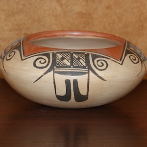 May include: A small, white ceramic bowl with a brown rim and black geometric designs. The bowl has a traditional Southwestern style.