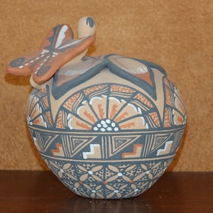 Op de afbeelding: Een handbeschilderde keramische pot met een vlinderontwerp. De pot is versierd met geometrische patronen in tinten bruin, zwart en wit.