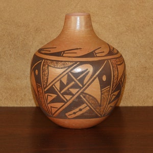 May include: A brown ceramic vase with a geometric design in black and brown. The vase has a rounded body and a narrow neck.
