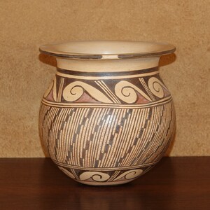 Può includere: Un vaso in ceramica marrone e bianco con un design geometrico. Il vaso ha un'ampia apertura e un corpo arrotondato.