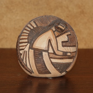 Puede incluir: Una olla redonda de cerámica marrón y blanca con un diseño tallado de una persona en un estilo tradicional nativo americano.
