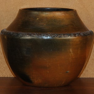 May include: A dark brown and black ceramic pot with a textured rim. The pot has a rounded shape and a smooth, glossy finish.