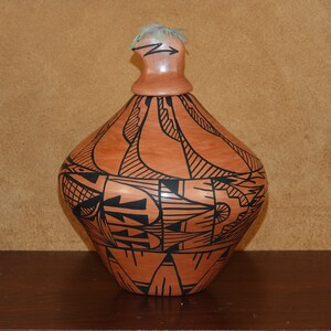 Op de afbeelding: Een bruine keramische pot met een zwart geometrisch ontwerp. De pot heeft een rond lichaam en een klein, rond deksel.
