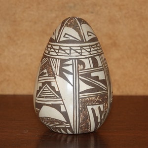 Op de afbeelding: Een witte keramische pot met een bruin geometrisch patroon. De pot heeft de vorm van een ei en heeft een gladde, glanzende afwerking.