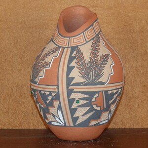 Op de afbeelding: Een handgeschilderde aardewerken vaas met een geometrisch en bloemmotief. De vaas is versierd met bruine, zwarte, witte en beige verf. De vaas heeft een brede opening en een rond lichaam.