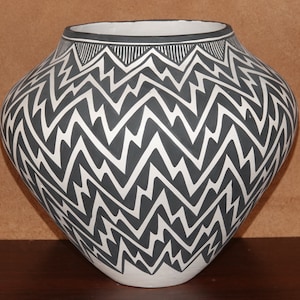 Op de afbeelding: Een witte keramische pot met een zwart-wit geometrisch patroon. Het patroon is een reeks zigzaggen en driehoeken.