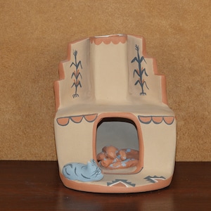 Könnte beinhalten: Eine Keramikfigur eines Pueblo-Hauses mit einer blauen Katze und zwei braunen Figuren im Inneren. Das Haus ist mit braunen, blauen und weißen Details bemalt.