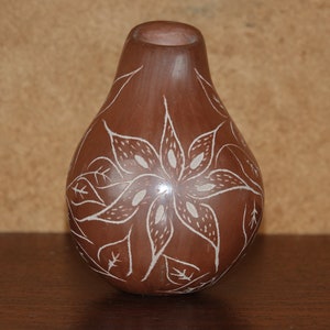Può includere: Un vaso di ceramica marrone con un motivo floreale bianco. Il vaso ha la forma di una pera e un collo stretto.