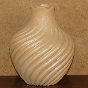 以下が含まれることがあります： 渦巻き模様のテクスチャが施された薄い茶色の陶器の花瓶。花瓶は幅広の底と細い首をしています。