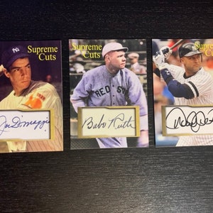 May include: Three baseball cards featuring the signatures of Joe DiMaggio, Babe Ruth, and Derek Jeter. Each card has a gold border and the text "Supreme Cuts" printed on it.