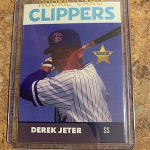 May include: A baseball card featuring Derek Jeter, a rookie player for the Clippers. The card is in a plastic case and features a photo of Jeter in a baseball uniform, holding a bat. The card is blue, white, and gold.
