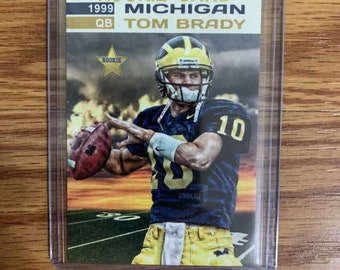 Puede incluir: Una tarjeta de novato con Tom Brady como mariscal de campo para la Universidad de Michigan. La tarjeta es dorada y azul con una imagen de Brady lanzando un balón de fútbol. La tarjeta tiene el texto "Rookie Card", "1999", "QB", "Michigan" y "Tom Brady".
