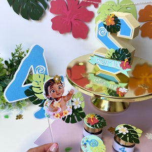 Pode incluir: Um topper de bolo azul com o n&uacute;mero quatro, um personagem de Moana, folhas verdes e um design de espiral. H&aacute; tamb&eacute;m pequenos frascos com o n&uacute;mero quatro e decora&ccedil;&otilde;es tropicais.