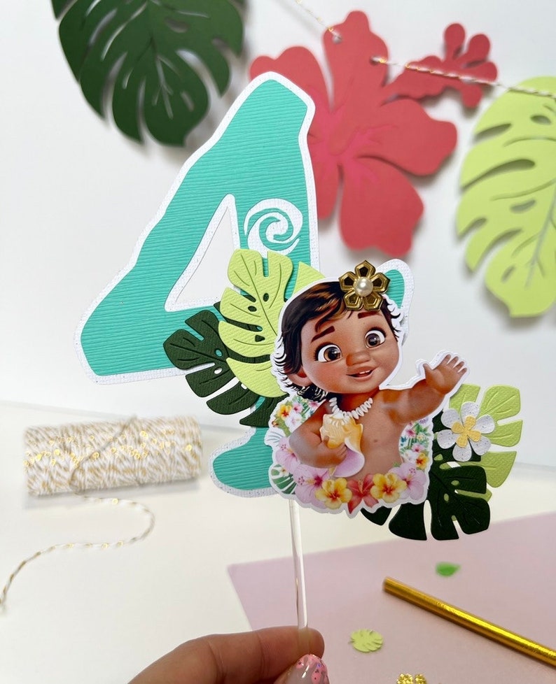 Pode incluir: Um topper de bolo de n&uacute;mero quatro verde com um personagem de Moana no centro. O personagem est&aacute; usando um colar de flores e segurando uma concha. O topper &eacute; cercado por folhas e flores verdes.