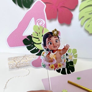 Pode incluir: N&uacute;mero quatro de papel rosa com um recorte de Moana do filme da Disney Moana, usando um colar de flores e segurando uma concha. O n&uacute;mero quatro &eacute; decorado com folhas e flores de papel verde.
