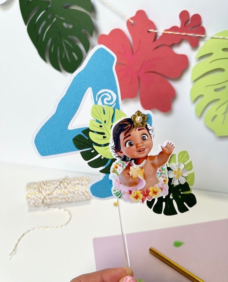 Pode incluir: Um topper de bolo de n&uacute;mero quatro azul com um tema tropical. O topper apresenta uma imagem de desenho animado de um beb&ecirc; Moana do filme da Disney Moana, cercado por folhas e flores verdes.