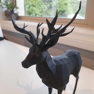 May include: A black, geometric deer sculpture with a detailed, angular antler design. The deer is standing on a white surface.