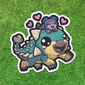 Puede incluir: Una pegatina de dibujos animados con un dinosaurio verde azulado y amarillo con una criatura púrpura más pequeña en su espalda, rodeada de corazones rosas. El dinosaurio tiene púas y una cara sonriente. La pegatina está sobre un fondo verde.