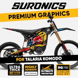 Op de afbeelding: Zwarte en gele elektrische motorfiets met Red Bull graphics. De afbeelding bevat de tekst "SURONICS PREMIUM GRAPHICS" en "FOR TALARIA KOMODO". Extra tekst omvat "ULTRA THICK 0,5 mm", "HIGHLY ADHESIVE", "ULTIMATE PROTECTION" en "HQ PRINT 8 COLOR 300 DPI".
