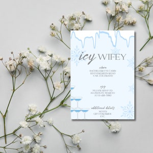 Op de afbeelding: Een blauwe en witte uitnodigingskaart met de tekst "icy WIFEY" en details voor een vrijgezellenfeest. De kaart heeft een sneeuwvlokkenontwerp en een stapel champagne glazen.
