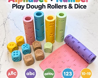 May include: A set of play dough rollers and dice featuring the text Alphabet + Number Play Dough Rollers & Dice. The collection includes cylindrical rollers in pink, blue, yellow, and green, alongside colourful dice and a pink flat mat.