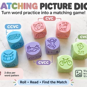 May include: A set of seven colourful educational dice in blue, pink, purple, and light green. Each die features engraved illustrations of objects like a sled, map, dog, lips, pond, person jumping, kite, drum, and bicycle, labelled with CVC, CCVC, CVCC, and CVCe text.