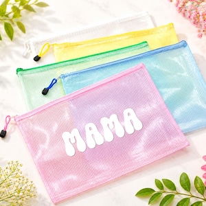 Puede incluir: Un conjunto de cinco estuches rectangulares de malla semitransparente con cremallera en blanco, amarillo, verde, azul y rosa. El estuche rosa presenta la palabra MAMA en letras blancas, gruesas y redondeadas. Cada estuche tiene un tirador a juego.