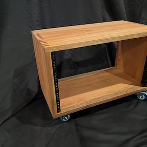 May include: A wooden rack with black metal rails for mounting audio equipment. The rack is on wheels and has a natural wood finish.