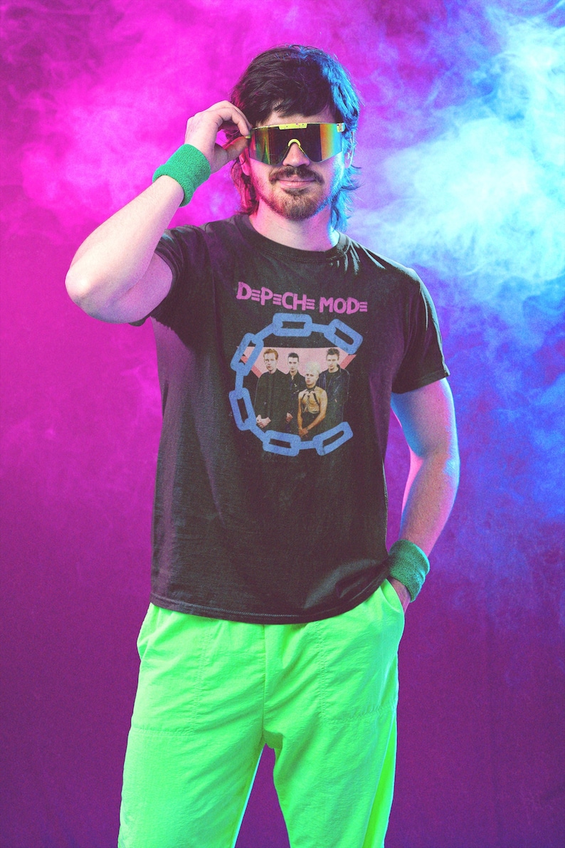 May include: A person wearing a black t-shirt with the band name "Depeche Mode" and a graphic of the band members. The person is also wearing neon green pants, a green wristband, and gold-rimmed sunglasses.