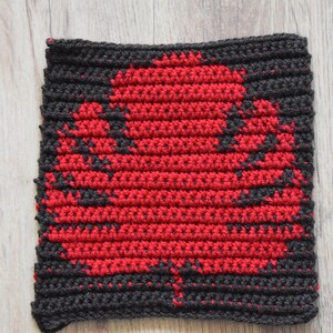 May include: A black and red crocheted square with a leaf design in the center.