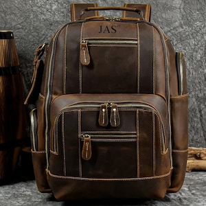 Może przedstawiać: Brązowy skórzany plecak z wieloma kieszeniami i zamkiem błyskawicznym. Plecak ma spersonalizowany napis "JAS".