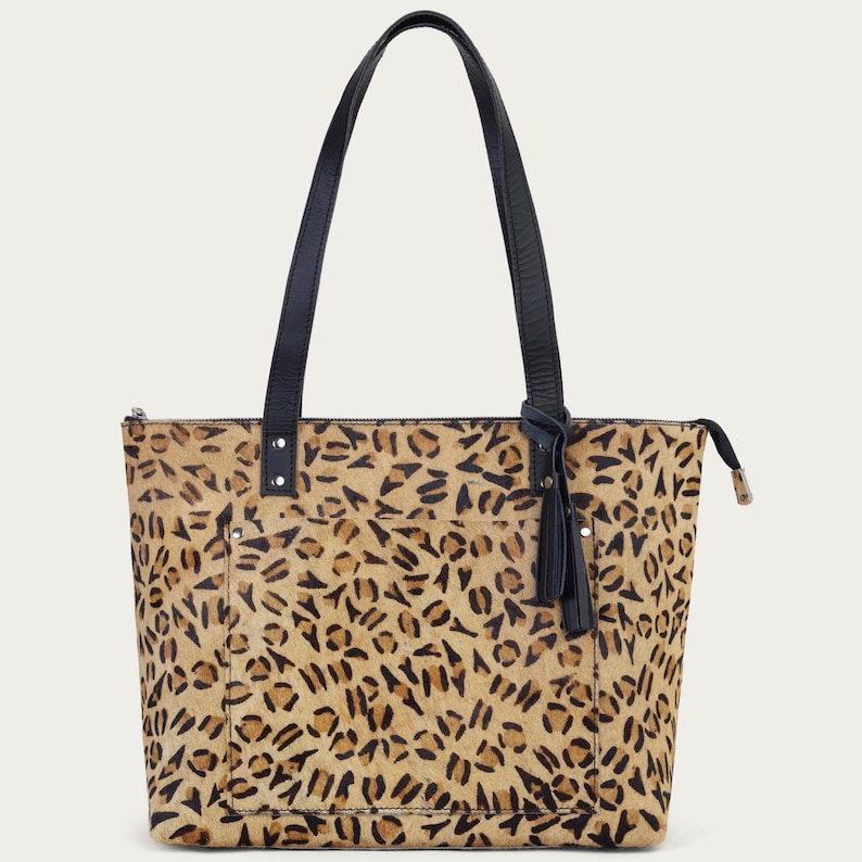 Peut inclure: Sac fourre-tout &agrave; imprim&eacute; l&eacute;opard marron et beige. Il est dot&eacute; de poign&eacute;es en cuir noir et d'un pompon noir. Le sac a une fermeture &eacute;clair.